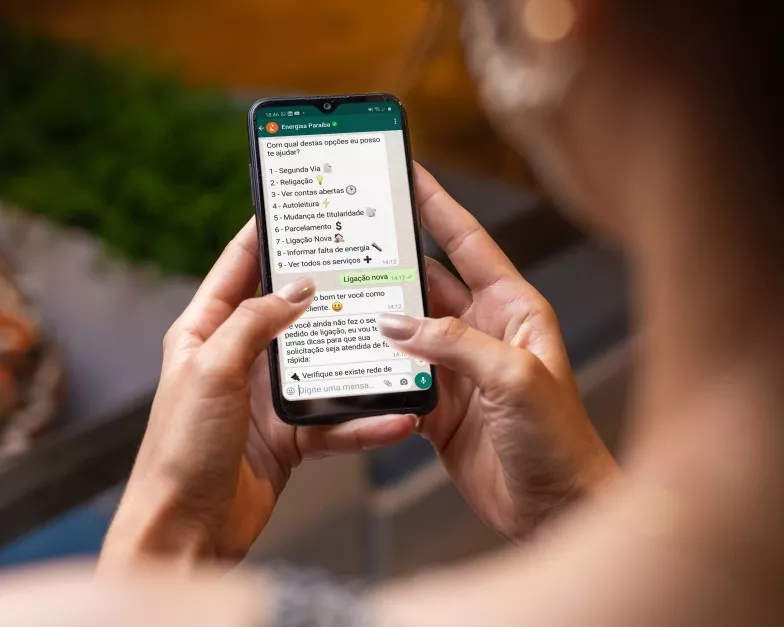 Mulher conversando com a Gisa, atendente virtual da Energisa, no WhatsApp em um telefone celular
