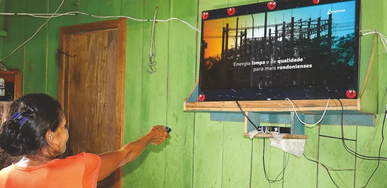 Mulher aponta o controle remoto para uma TV com um anúncio da Energisa